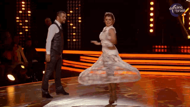 a woman in a white dress is dancing with a man in a black vest