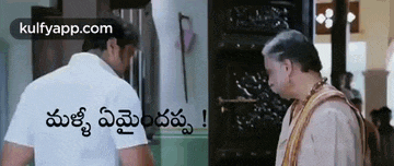 a man in a white shirt is talking to another man in a room .