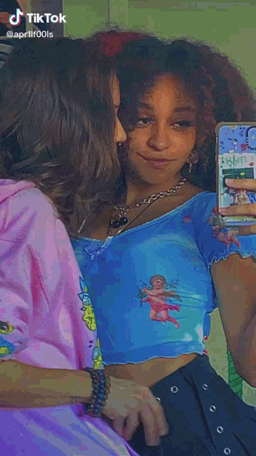 a woman is taking a selfie in front of a mirror while wearing a pink hoodie and a blue crop top .