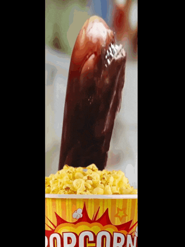 a bucket of popcorn with a hot dog sticking out of the top
