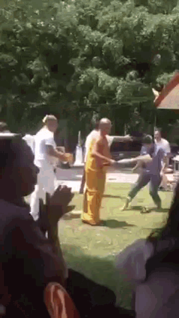 a group of people are standing around a man in a yellow robe who is standing in the grass .