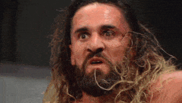 a man with long hair and a beard is making a surprised face .