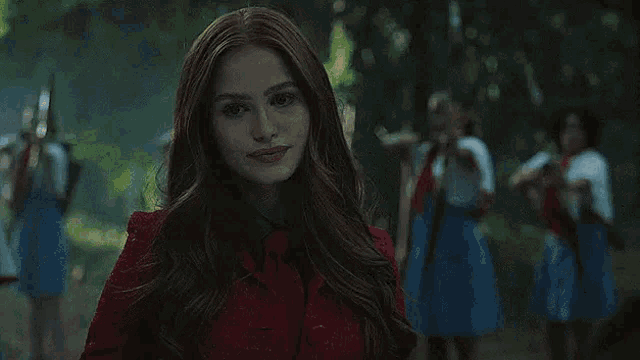 a close up of a woman in a red dress looking at the camera in a dark forest .