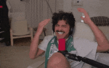 a man wearing headphones is sitting in a chair and laughing while holding a red cell phone .