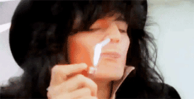 a woman with long black hair is smoking a cigarette with a lighter .