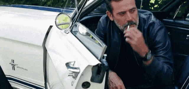 a man with a mustache is smoking a cigarette while sitting in a white car .
