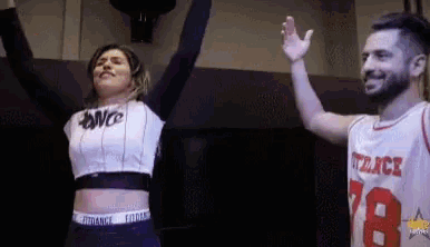 a man and a woman are standing next to each other with their arms up .