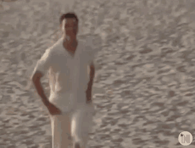a man in a white shirt is running on a beach holding a tennis racket .