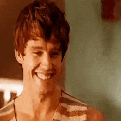 a young man in a striped tank top is smiling and looking at the camera .