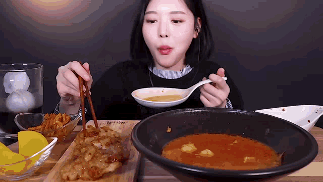 a woman is eating a bowl of soup with chopsticks and a spoon