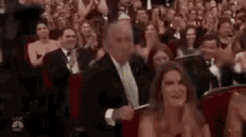 a man in a suit and tie is giving a thumbs up to a woman in a red dress in a crowd of people .