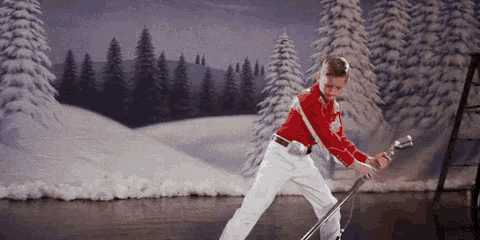 a boy in a red shirt is holding a microphone in front of a snowy scene