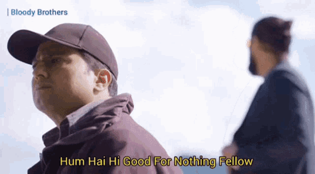 a man in a baseball cap says " hum hai hi good for nothing fellow " while standing next to another man