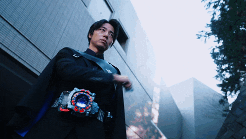 a man wearing a cape and a belt with a circle on it is standing in front of a building