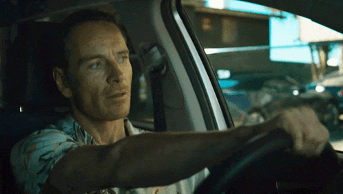 a man in a blue shirt is driving a white car