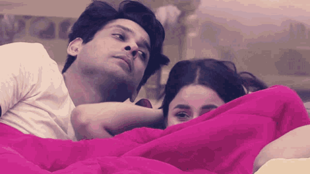 a man and a woman are laying in bed under a pink blanket