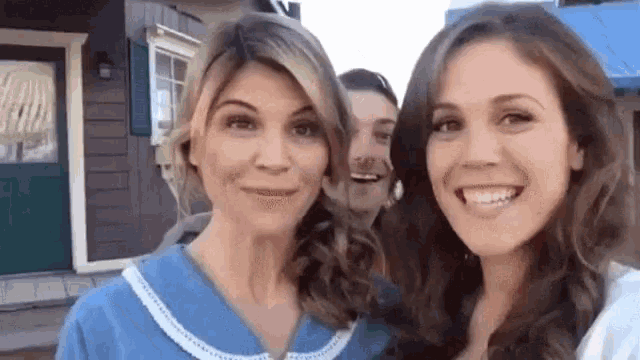 three women are posing for a picture in front of a building .