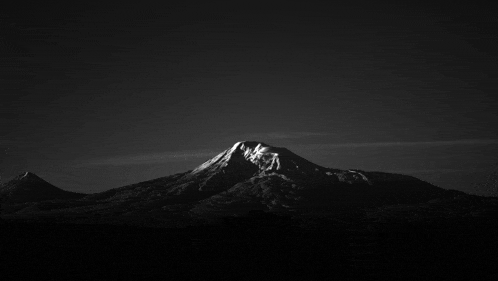 a black and white photo of a mountain with a dark sky in the background