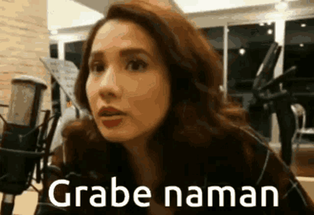 a woman is standing in front of a microphone with the words grabe naman written on her face .