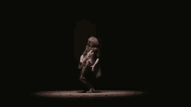 a man in a black leather jacket is playing a red electric guitar in the dark .