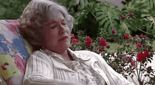 an elderly woman is sleeping on a couch in a garden .