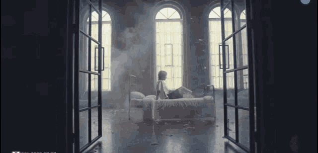 a man is sitting on a bed in a room with a lot of windows
