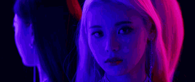 a close up of a woman 's face in a dark room with purple and pink lights behind her .