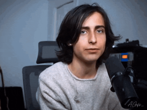 a young man with long hair is sitting in front of a microphone with the letters agts on the bottom right