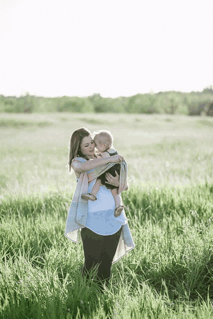 a woman holds a baby in her arms in a grassy field