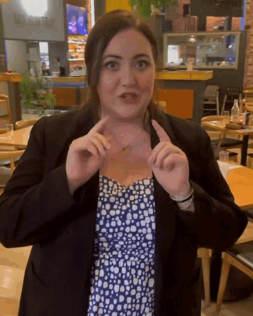 a woman wearing a black jacket and a blue and white polka dot dress stands in a restaurant
