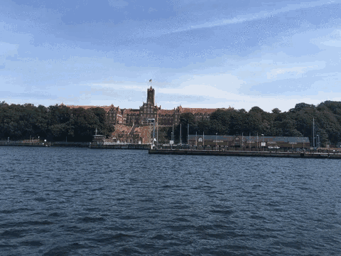 a large brick building with a flag on top of it sits on a hill overlooking a body of water