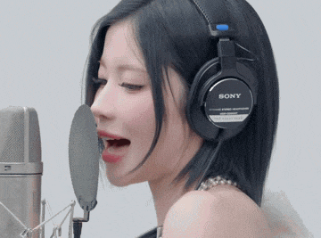 a woman wearing a pair of sony headphones is singing into a microphone