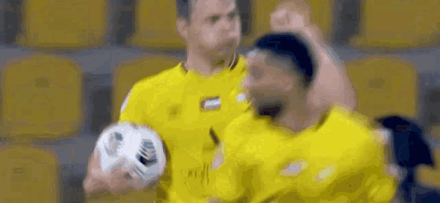 two men in yellow jerseys are holding a soccer ball and celebrating .