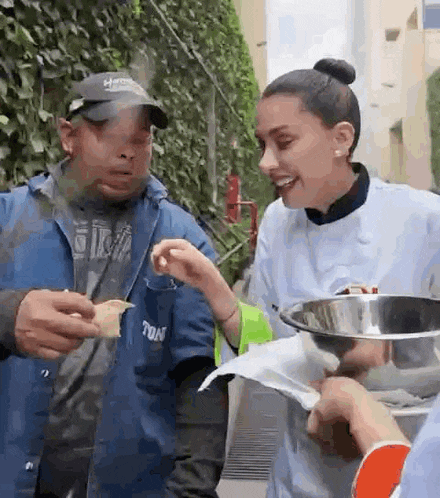 a man and a woman are standing next to each other eating food from a bowl .