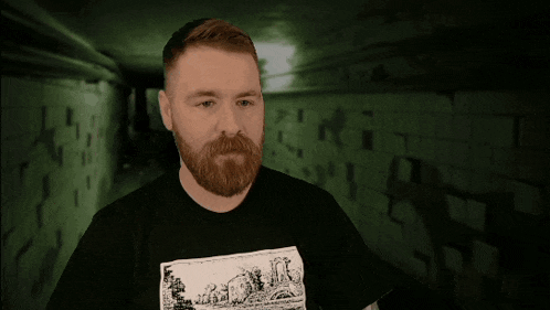 a man with a beard is wearing a black shirt with a picture of a cartoon on it