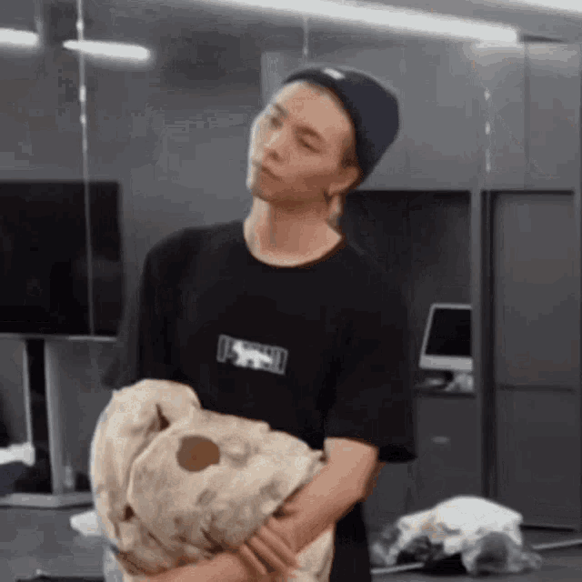 a man in a black t-shirt is holding a stuffed animal in his arms .