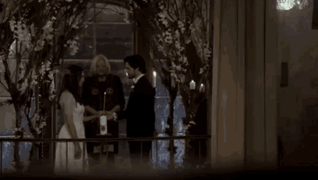 a bride and groom are standing on a balcony holding hands with a priest .