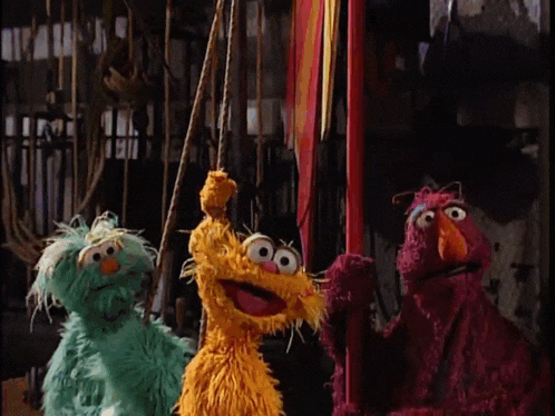 a group of sesame street stuffed animals are standing next to each other on a swing .