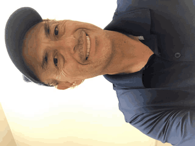a man wearing a black hat and a blue shirt smiles