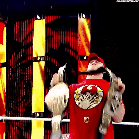 a wrestler in a red shirt is holding a championship belt .