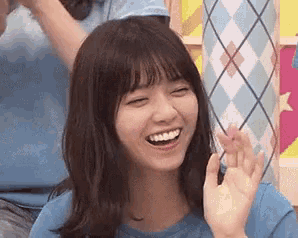 a woman in a blue shirt is smiling with her eyes closed and waving .
