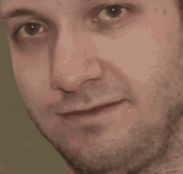 a close up of a man 's face with a beard and a smile on his face .