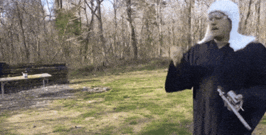 a man in a black robe holding a gun in a field