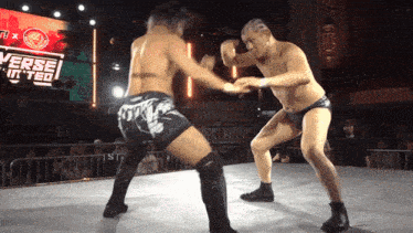 two men are wrestling in front of a large screen that says verse on it