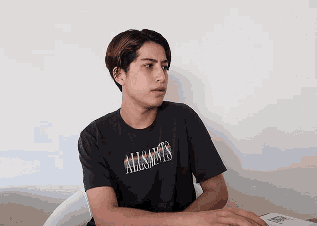 a man wearing an allsaints t-shirt sits in a chair