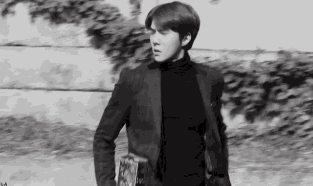 a black and white photo of a man in a suit and turtleneck walking down a street .