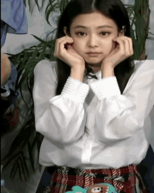 a girl with her hands on her face is wearing a white shirt