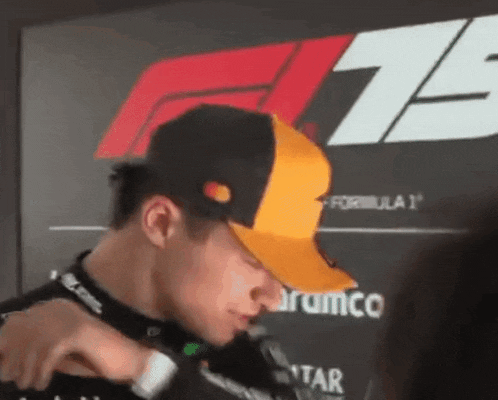 a man wearing a yellow and black baseball cap is standing in front of a sign that says formula 1