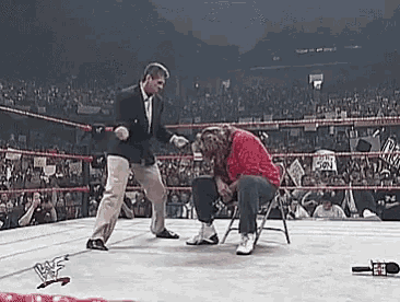 a man in a suit is standing next to a man in a red shirt in a wrestling ring .