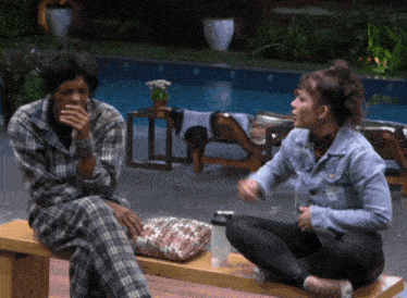 a man and a woman are sitting on a bench in front of a swimming pool